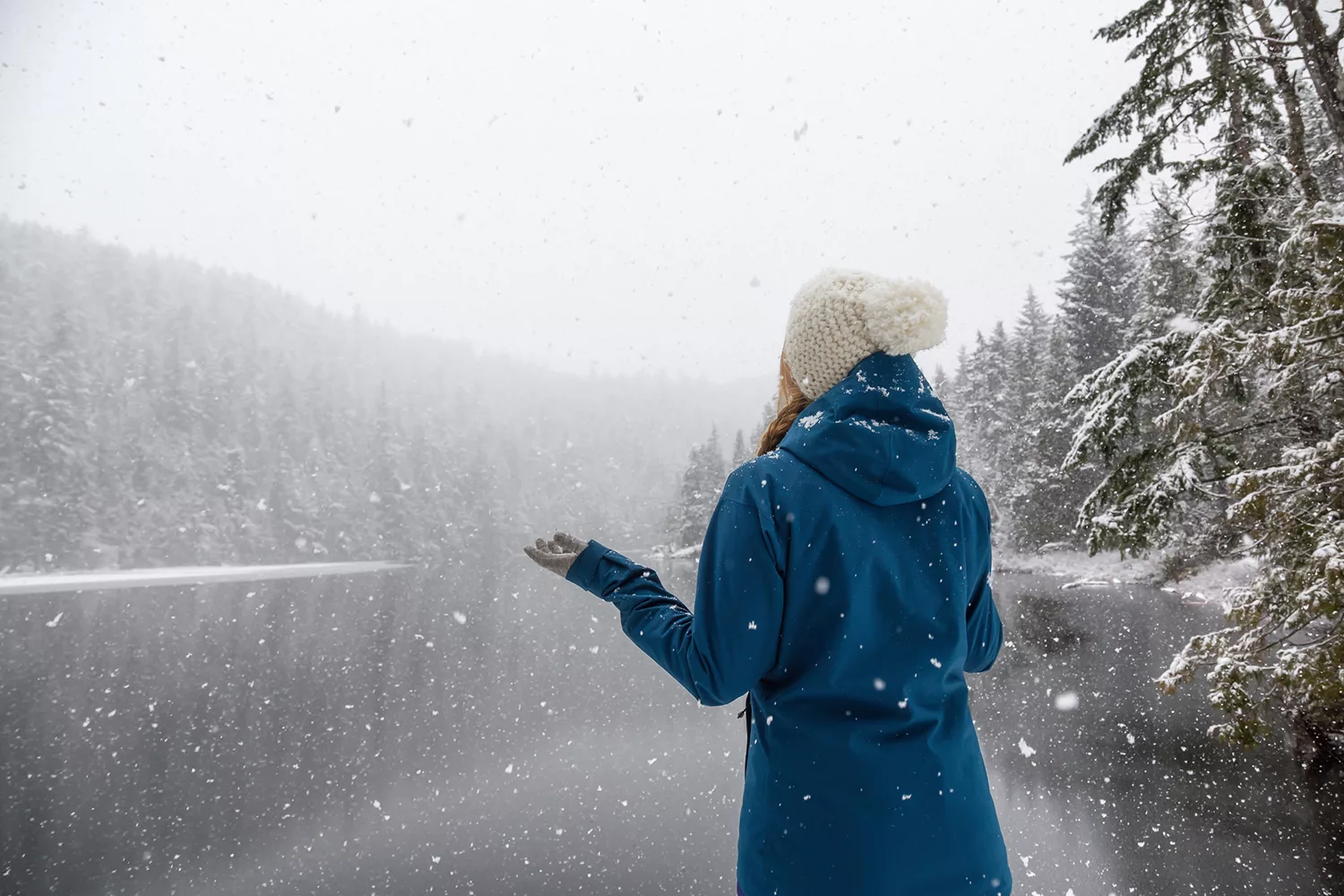 Woman by the icy lake Explore Magazine Woman enjoying the beautiful Canadian Winter Landscape during a snowy day. Taken near Squamish and Whistler, North of Vancouver, BC, Canada.